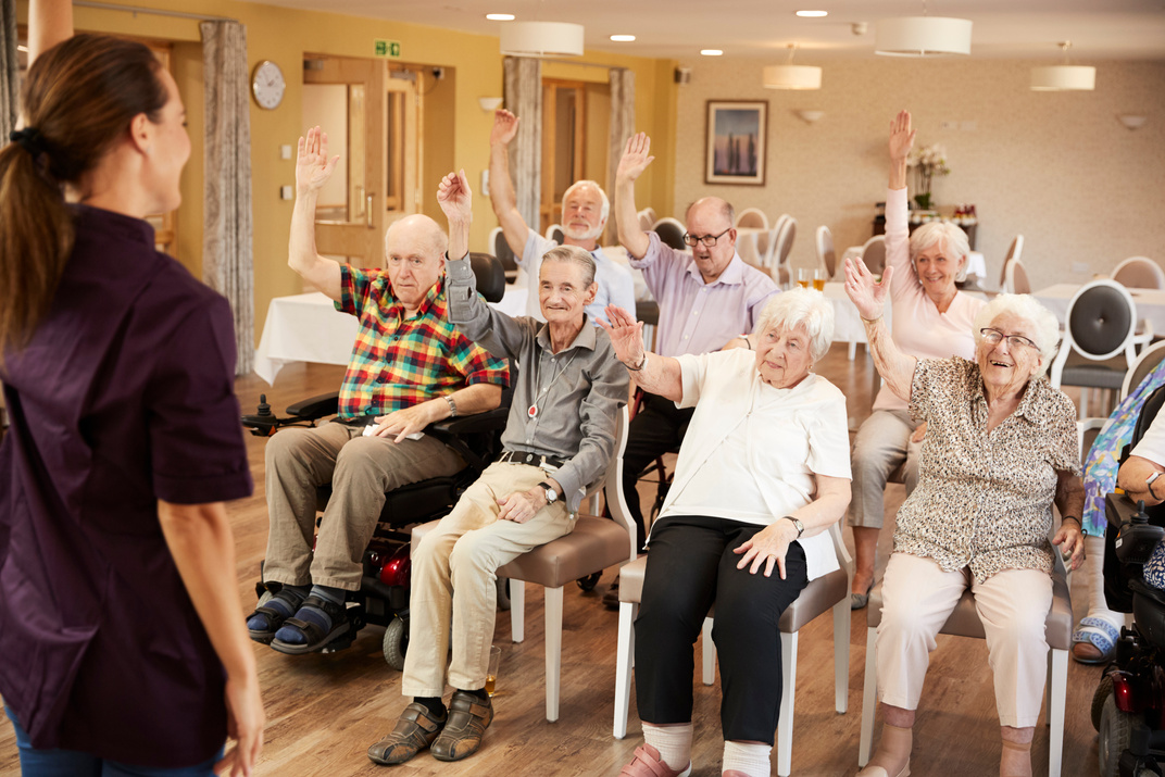 Carer Leading Group of Seniors in Fitness Class in Retirement Ho